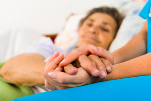 Blurred photo of a medical professional holding the hand of a woman laying in a bed