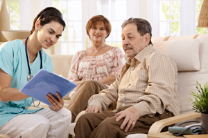 Photo of a medical professional sitting beside and older man and woman reviewing information on a clipboard.