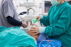 Photo of two medical professionals performing a medical procedure on a patient laying on an operating table