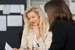 A smiling woman sitting down reviewing a piece of paper with another woman.