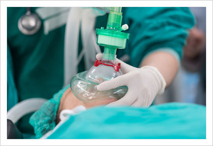 Photo of a medical professional holding a breathing apparatus to the mouth of a patient lying on an operating table